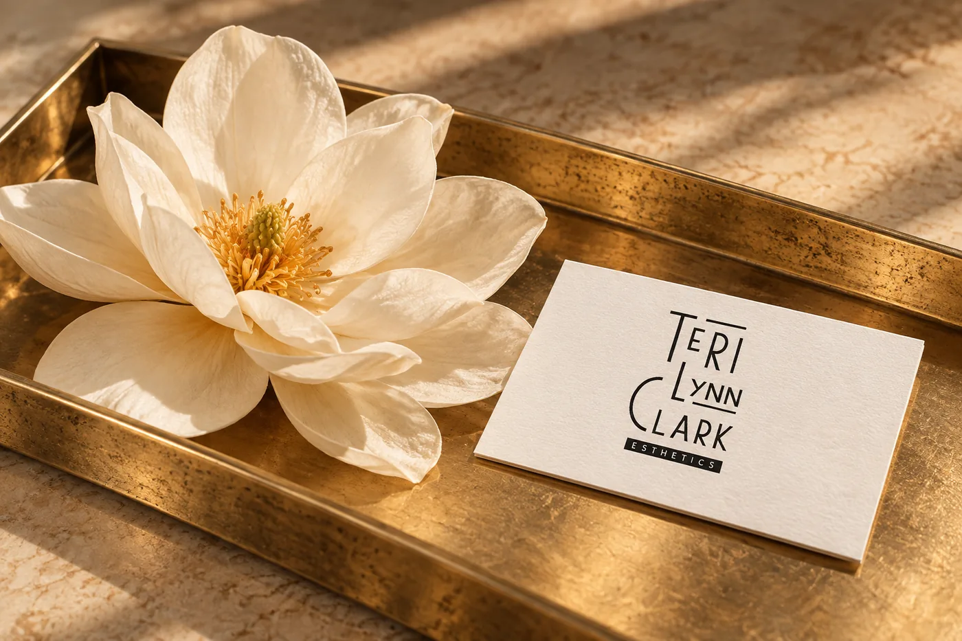 A white lotus flower and a Teri Lynn Clark business card on a gold tray